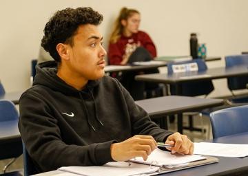 Accounting student sits, attentive in class with pen and paper